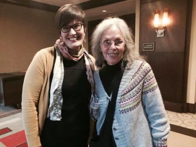 Two women smiling in a conference setting.