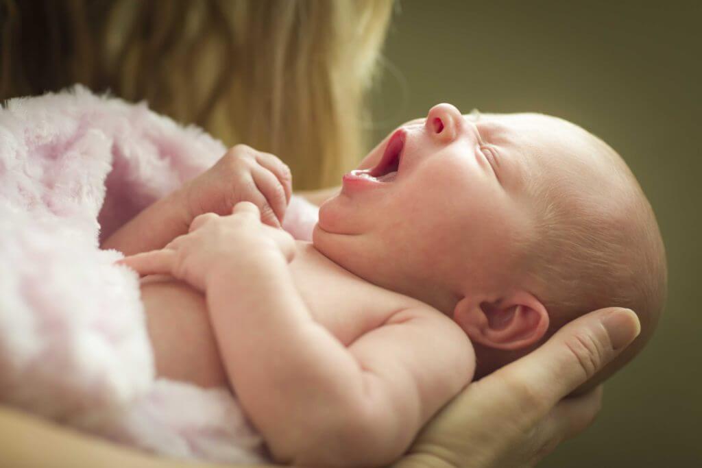 Newborn baby yawning in parent's arms.