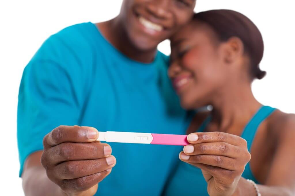 Couple holding positive pregnancy test, smiling together.