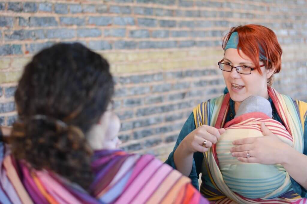 Women discussing babywearing with colorful wraps.