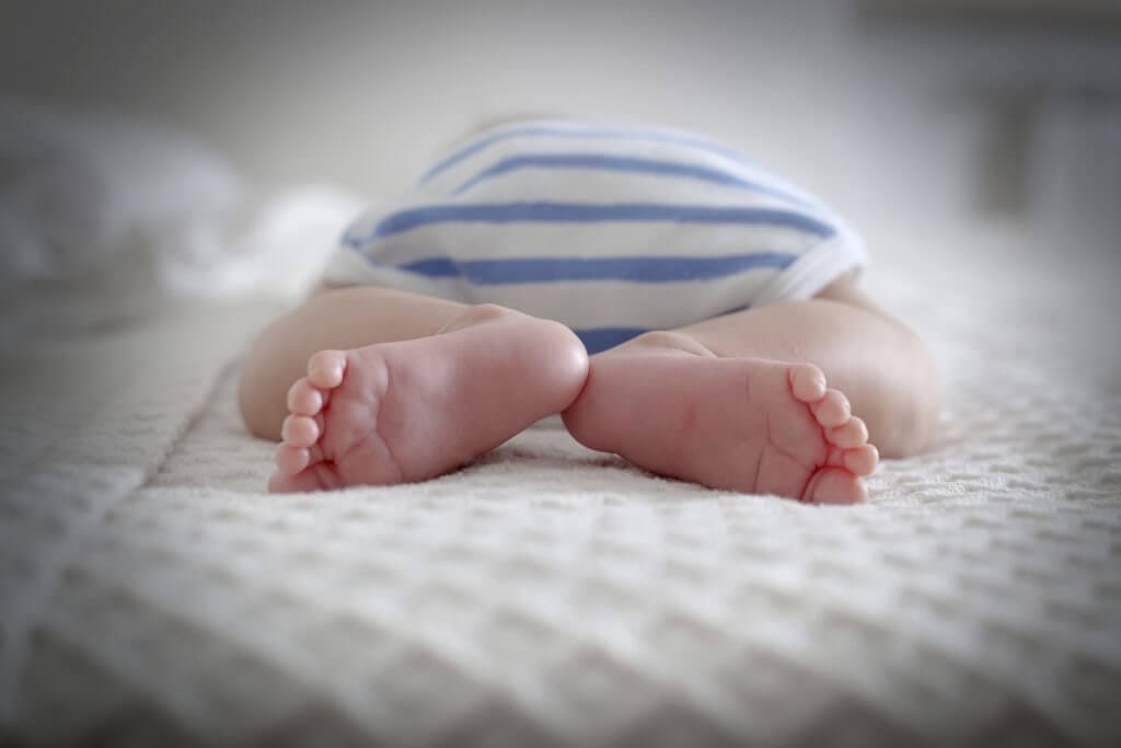 Baby laying on bed in striped outfit.