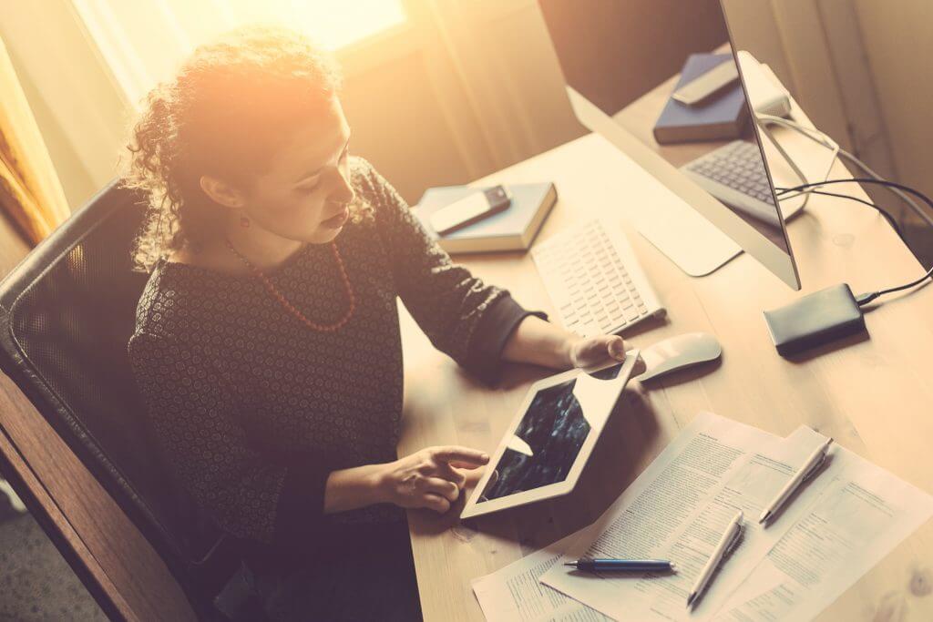 Woman working on tablet at desk with documents.