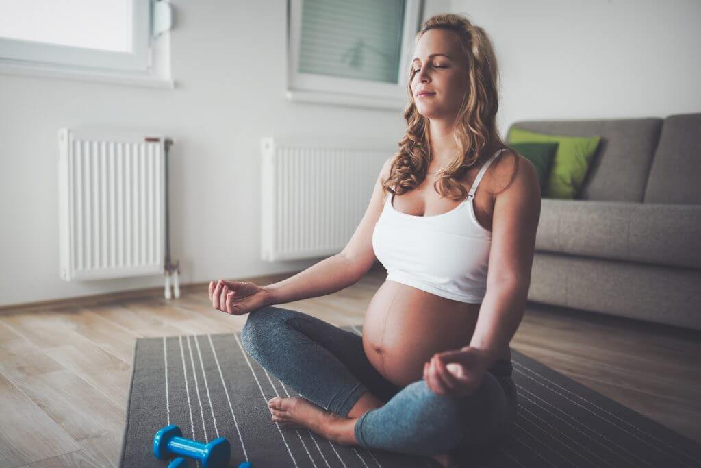 Pregnant woman meditating on yoga mat at home.