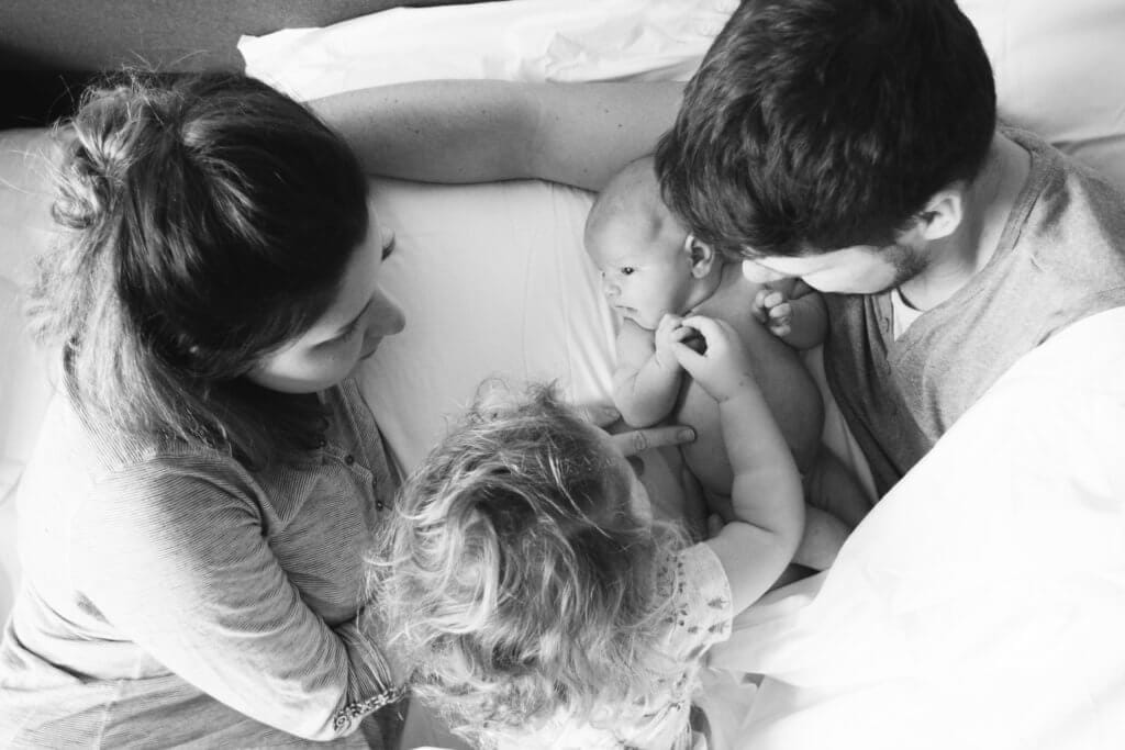 Family with baby and toddler on bed.
