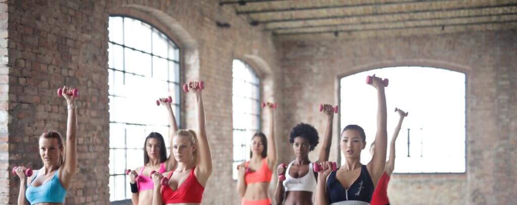 Women exercising with dumbbells in a gym.