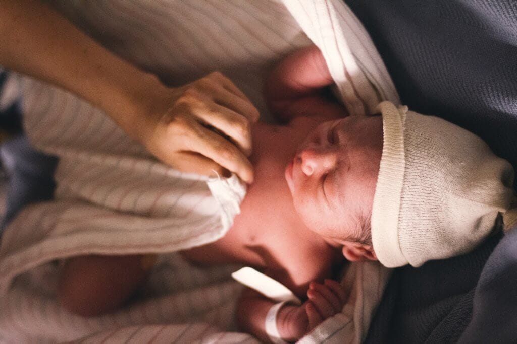 Newborn baby under a blanket with knitted hat.