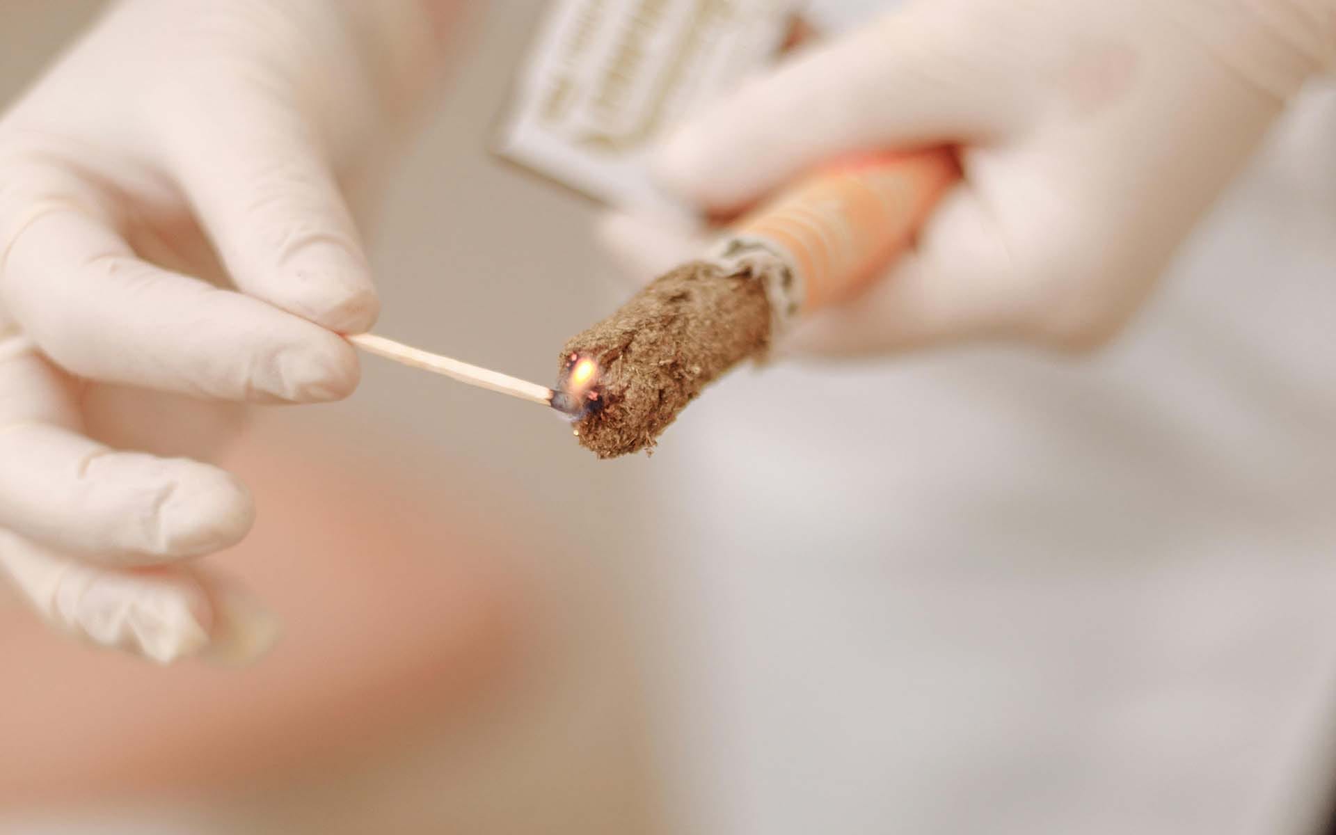 Gloved hands lighting incense stick with match.