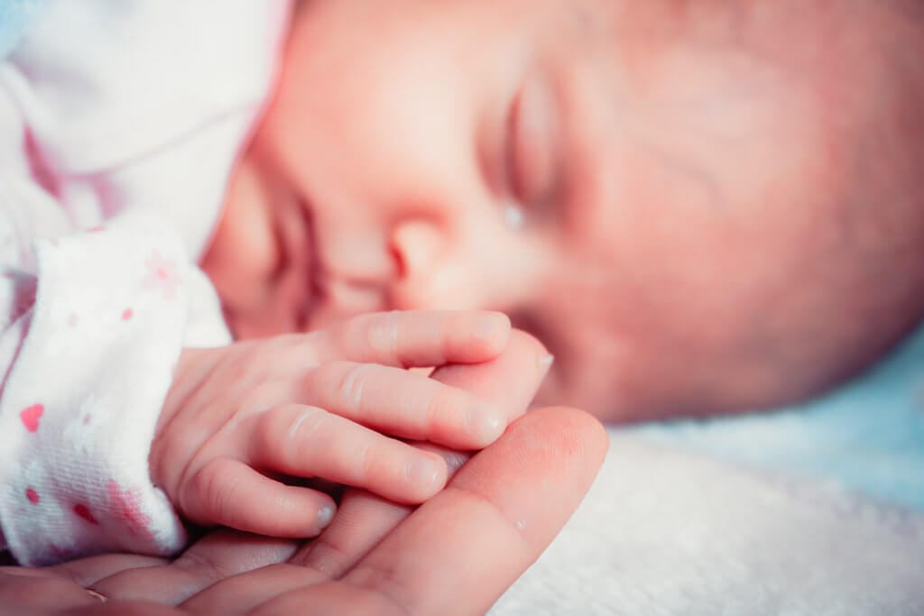 Sleeping baby holding adult's finger