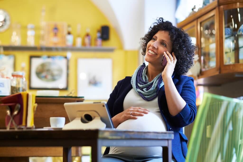 Pregnant woman happily talking on phone in cafe.