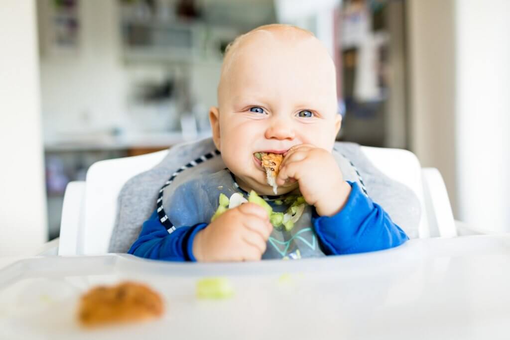 Baby eating in high chair, smiling.