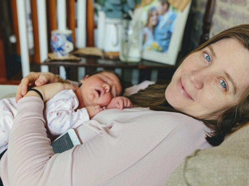 Mother and newborn baby cuddling on couch.