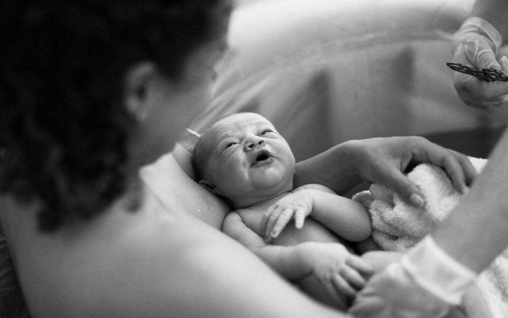 Newborn in water, mother holding gently.