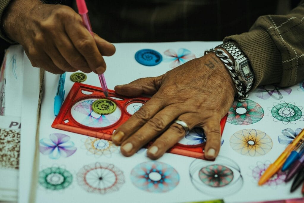 Close-up of hands creating vibrant spirograph patterns with pencils, showcasing creativity and precision.