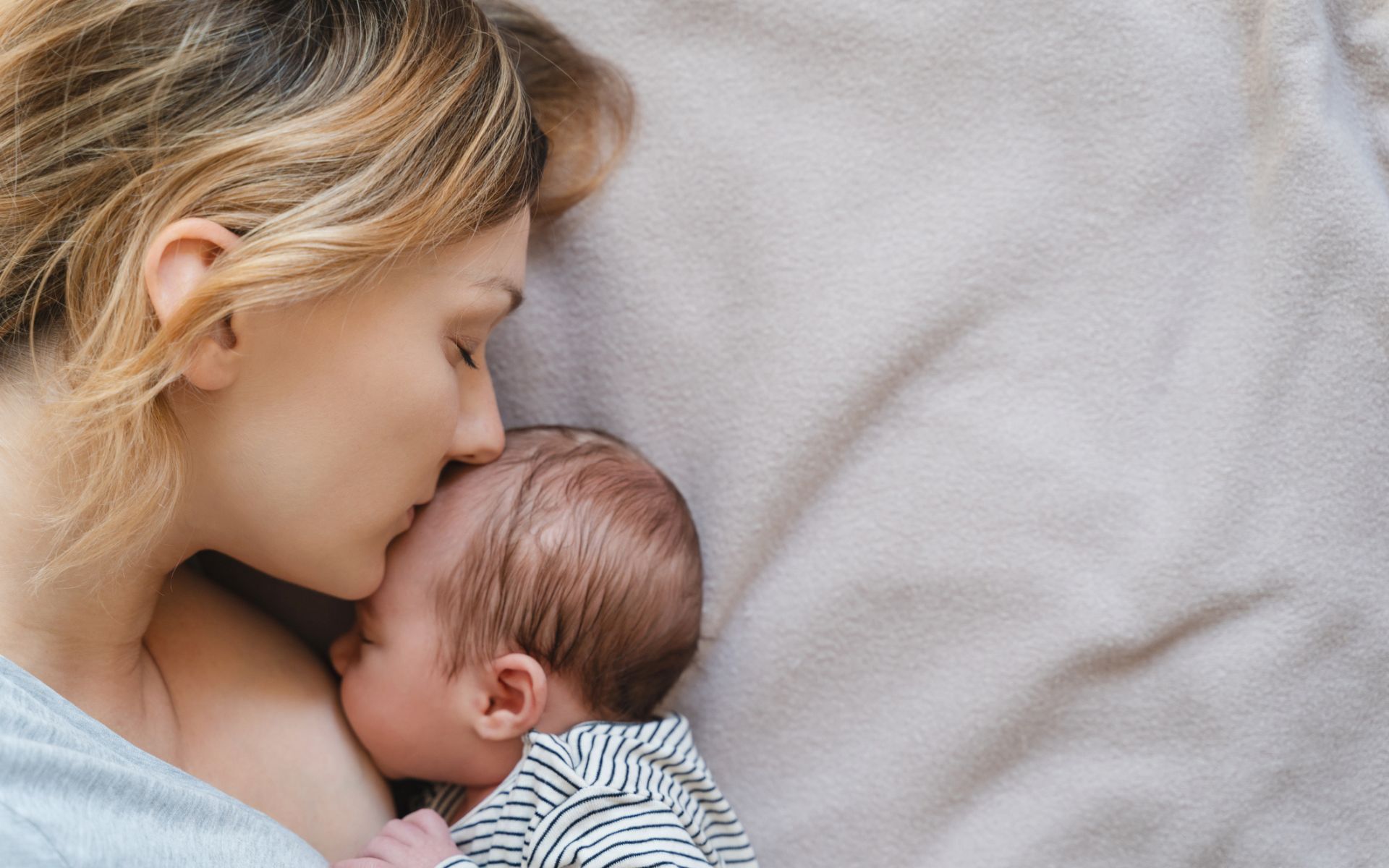 Postpartum woman kissing the top of her newborns head while she waits for her placenta encapsulation in San Antonio