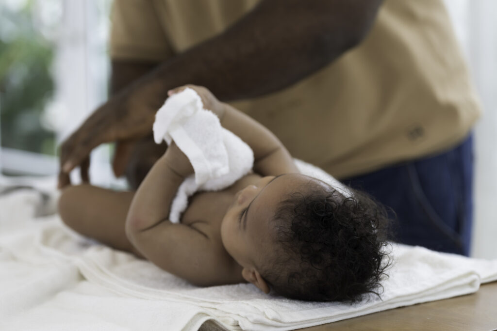 African American father and cute baby toddler. Father cleaning and health newborn child, wearing newborn baby diaper after taking shower